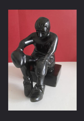 Das Bild zeigt eine schwarze Specksteinskultur: ein sitzender Boxer mit offenem Schnürsenkel.