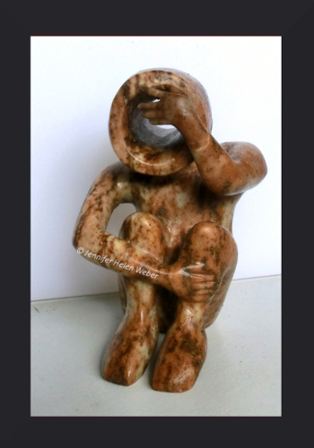 Die Specksteinfigur zeigt einen Kriegswaisen: ein sitzender Junge, der sich die Hand vor die Augen hält.