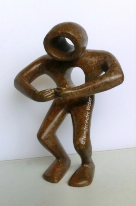 Das Bild zeigt eine braune Specksteinfigur. eine Person, die ein Loch im Herzen hat, das sie mit den Armen zu schützen versucht