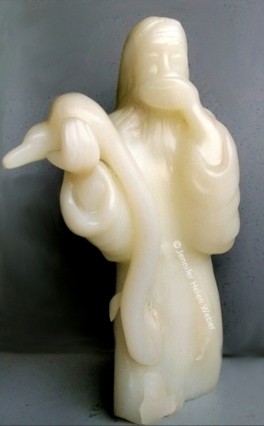 Die weisse Specksteinfigur zeigt eine bärtige Figur, die eine Schöpferfigur (Gott) darstellen soll. Sie hält eine grosse Schlange in der Hand, die den Erdball komplett verschluckt hat und hält sich erschrocken eine Hand vor den Mund.