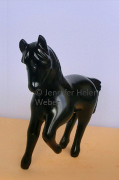 Das Bild zeigt eine schwarze Specksteinfigur: die Seitenansicht einer Stute, die angetrabt kommt.