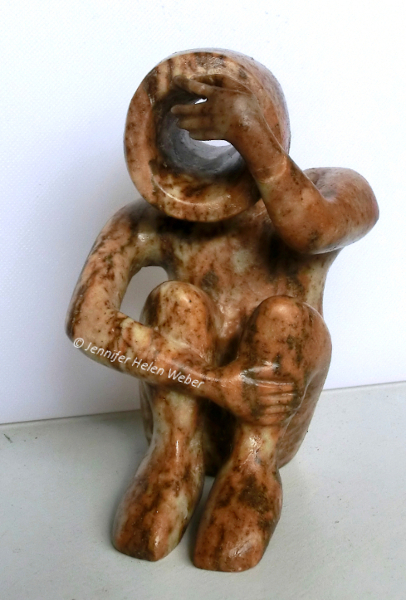 Die Specksteinfigur zeigt einen Kriegswaisen: ein sitzender Junge, der sich die Hand vor die Augen hält.