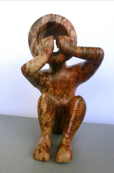 Die Specksteinfigur zeigt einen sitzenden Junge, der die Hände ängstlich und entsetzt vor den Mund hält.